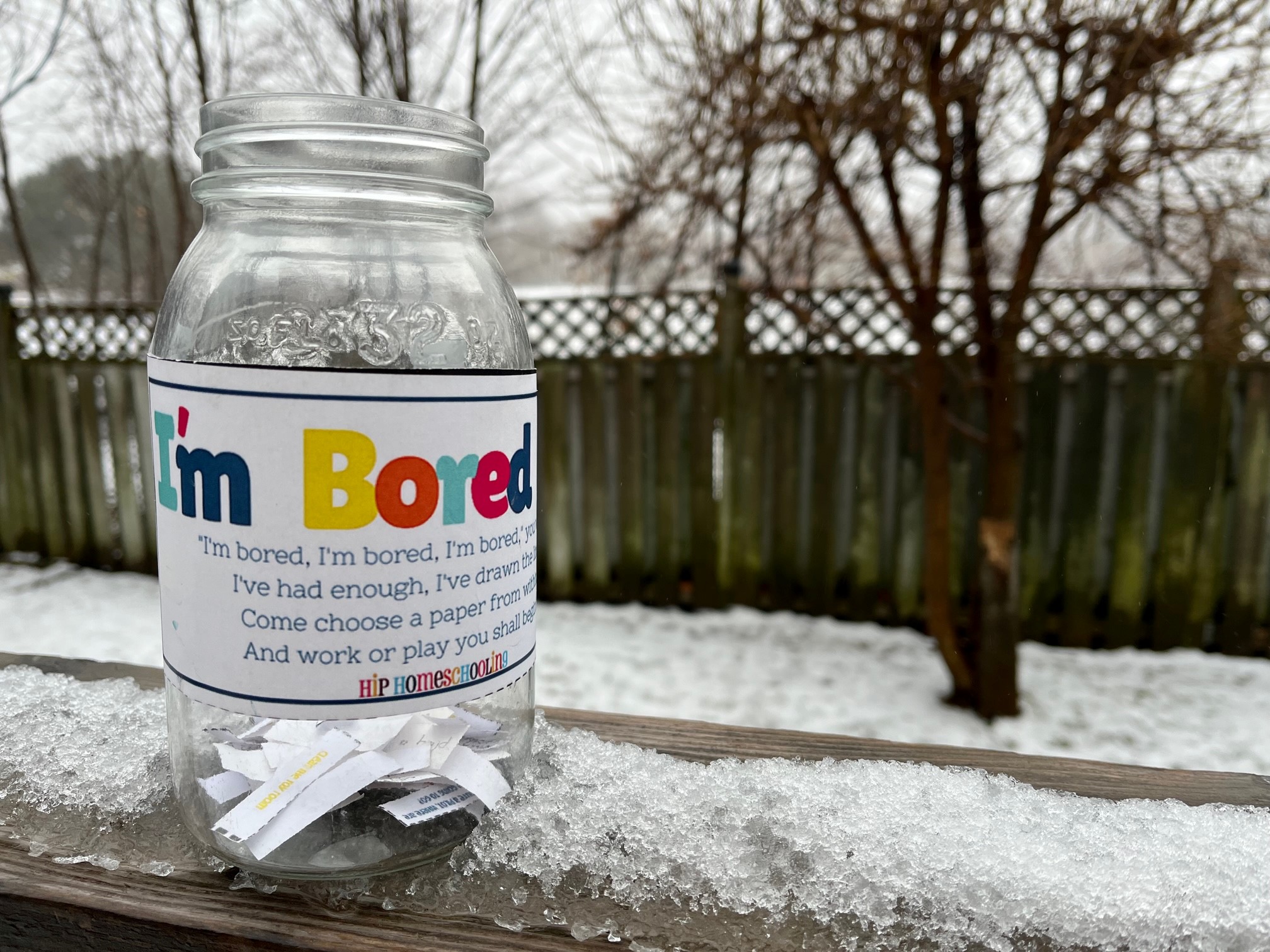 A mason jar, with a label reading "I'm Bored Jar", is filled with slips of paper with activity ideas on them